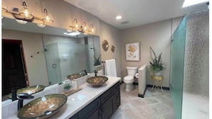 Une salle de bain comprenant un grand miroir, un lavabo avec un receveur, des toilettes et un espace douche.