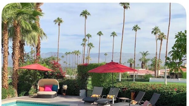 Un espace piscine avec des chaises longues, un foyer et des parasols rouges.