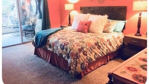 Une chambre à coucher avec un lit, deux lampes de chevet, une tête de lit et une vue sur l’extérieur à travers une porte vitrée.
