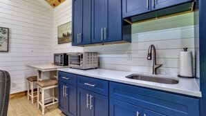Een keuken met blauwe kastjes, een magnetron, een broodrooster en een spoelbak.