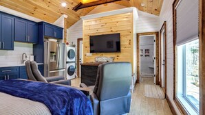 Een compacte kamer met een bed, bureau, stoel, televisie en kitchenette.