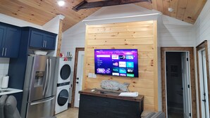 Een moderne keuken met roestvrijstalen apparatuur, een ingebouwde wasmachine en droger, en een flatscreen televisie bevestigd aan een houten wand.