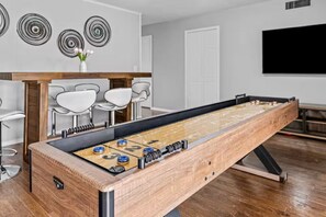 A foosball table in a room with a wooden floor, white walls, and a flat-screen TV mounted on the wall.