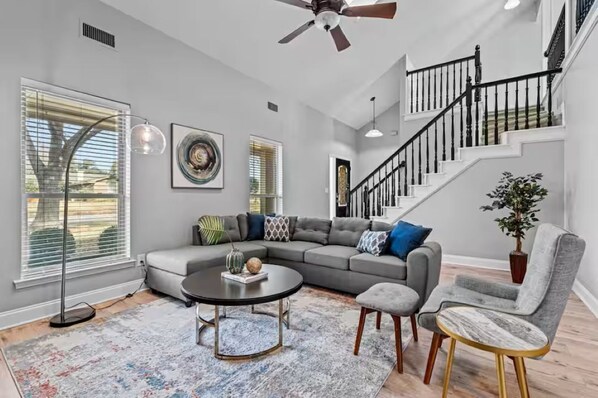A modern living room with a gray sectional sofa, a round coffee table, and a staircase with black railings.