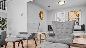 Ein modernes Wohnzimmer mit grau gepolsterten Sesseln, einem runden Couchtisch und einer Treppe, die in ein Obergeschoss führt.
