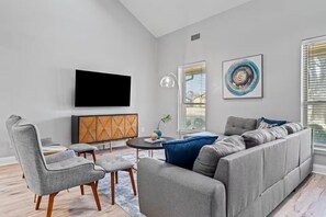 A modern living room with a sectional sofa, a flat-screen TV, a wooden cabinet, and two abstract paintings.