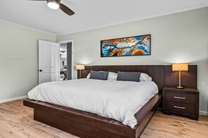 A bedroom with a bed, bedside tables, a ceiling fan, and a painting on the wall.