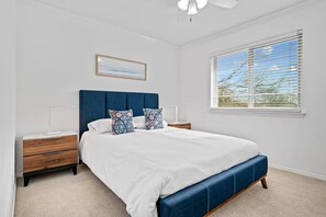 A bedroom with a bed, nightstands, a ceiling fan, a window with blinds, and a framed picture on the wall.