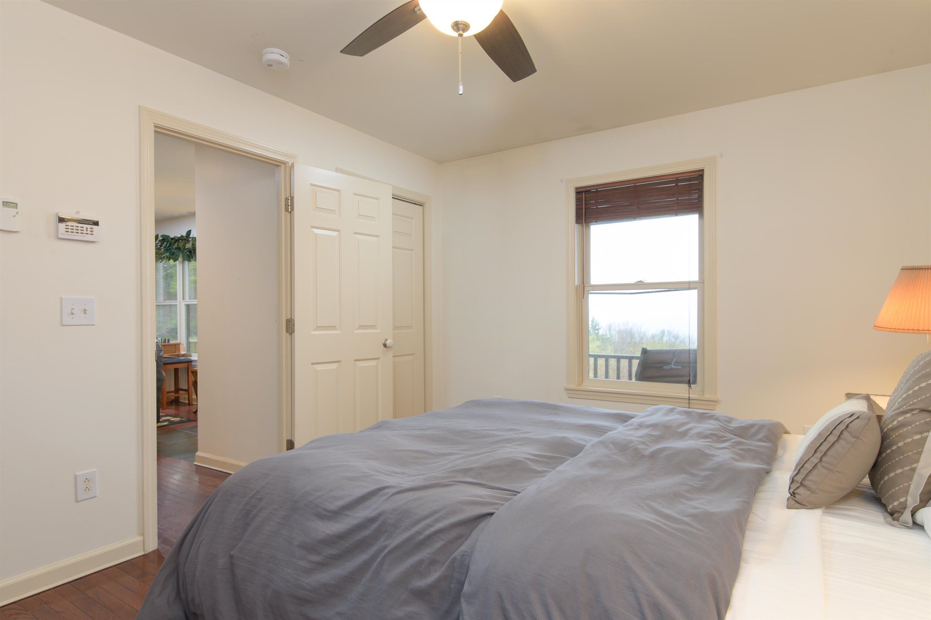 A bedroom with a bed, a ceiling fan, a window with blinds, and a door leading to another room.