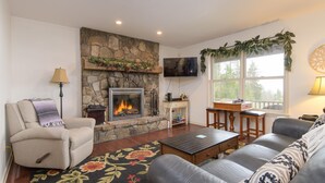 A living room with a stone fireplace, a sofa, a coffee table, and a television mounted on the wall. - Mountain View Retreat (Ludlow)