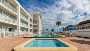 A hotel with a swimming pool, multiple balconies, and outdoor seating areas. - Delightful, Cozy Modern Apartment By The Ocean @Coastal Waters (New Smyrna Beach)