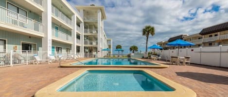 Un hotel con piscina, varios balcones y zonas de estar al aire libre.