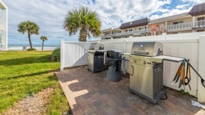 An outdoor patio with a grill, a trash can, and a fence. - Delightful, Cozy Modern Apartment By The Ocean @Coastal Waters (New Smyrna Beach)