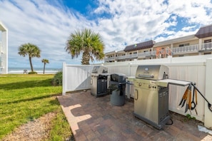 An outdoor patio with a grill, a trash can, and a fence. - Delightful, Cozy Modern Apartment By The Ocean @Coastal Waters (New Smyrna Beach)