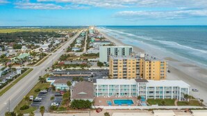 An aerial view of a coastal town with a beachfront hotel, roads, and surrounding greenery. - Delightful, Cozy Modern Apartment By The Ocean @Coastal Waters (New Smyrna Beach)