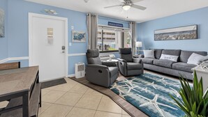 A living room with a gray sofa, a gray armchair, a ceiling fan, and a blue rug with starfish design. - Delightful, Cozy Modern Apartment By The Ocean @Coastal Waters (New Smyrna Beach)