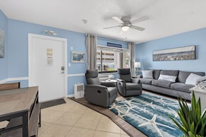 A living room with a gray sofa, a gray armchair, a ceiling fan, and a blue rug with starfish design. - Delightful, Cozy Modern Apartment By The Ocean @Coastal Waters (New Smyrna Beach)