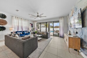 A modern living room with a grey sofa, a coffee table, and a TV on a wall. - 6BR Stylish Reunion Villa • Pool • Near Disney (Reunion)