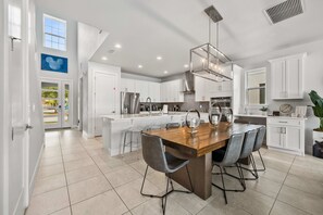 A modern kitchen with white cabinetry, a central island with bar stools, stainless steel appliances, and a large window providing natural light. - 6BR Stylish Reunion Villa • Pool • Near Disney (Reunion)