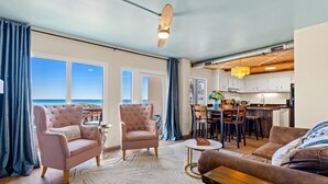 A living room with a sofa, armchair, and dining area with a view of the ocean. - Ocean Views, Pinnacle Port A-108 (Panama City Beach)