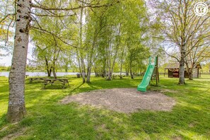 Ein Park mit Picknicktischen, einer Spielplatzanlage mit einer Rutsche und einem kleinen Gebäude.