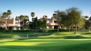 Un parcours de golf avec un mât de drapeau, des palmiers et un bâtiment doté de plusieurs balcons.