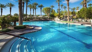 Une grande piscine extérieure entourée de palmiers et de chaises longues.