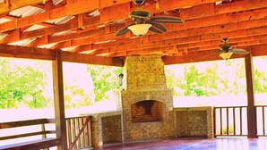 Un pabellón abierto con chimenea de piedra, vigas de madera y ventiladores de techo.