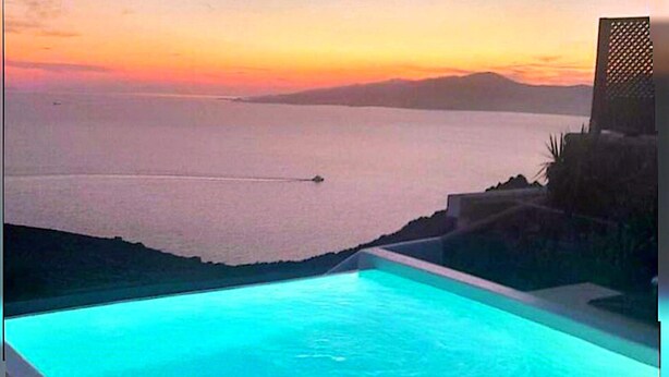 Ein Swimmingpool mit Blick auf das Meer und ferne Berge bei Sonnenuntergang.