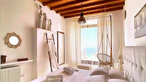 Ein Schlafzimmer mit Holzboden, einem Bett mit weißen Leinen, einem Hängekorbstuhl und einem Fenster mit Vorhängen.