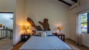 Um quarto com uma cama grande, cabeceira de madeira, duas mesas de cabeceira com luminárias e uma janela com cortinas.