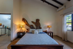 Ein Schlafzimmer mit einem großen Bett, einem Holz-Kopfteil, zwei Nachttischen mit Lampen und einem Fenster mit Vorhängen.