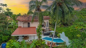 Uma casa com telhado de azulejos, piscina e vegetação exuberante.
