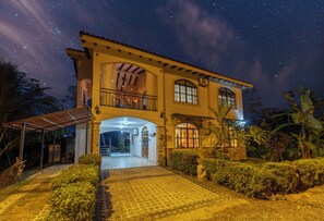 Ein zweistöckiges Haus mit Balkon, überdachter Veranda und einer Fassade aus Naturstein.