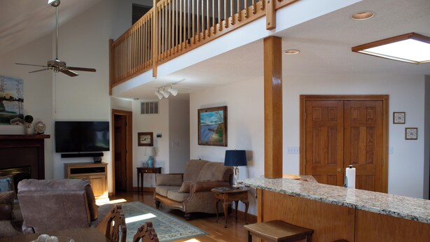A spacious living area with a high ceiling, a dining table with chairs, a sofa, a television, and a kitchen area with a countertop and bar stools.