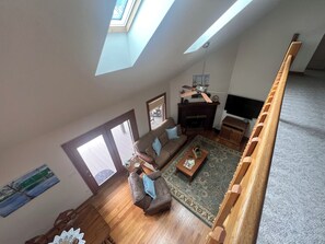 Ein Wohnzimmer mit hohen Decken, einem Oberlicht, einem Kamin, einem Fernseher und einer Holztreppe.
