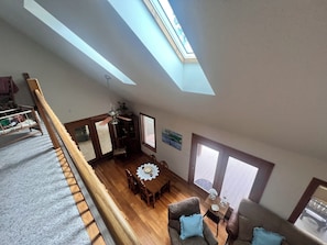 Ein Loft-Zimmer mit hohen Decken, einem Oberlicht, Holzboden, einem Esstisch und einer gemütlichen Sitzecke.