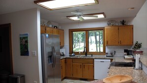 A kitchen with wooden cabinets, a stainless steel refrigerator, a dishwasher, and a large window.
