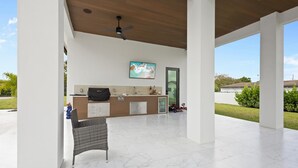 Un patio techado con una zona de estar, una encimera de cocina y un ventilador de techo.