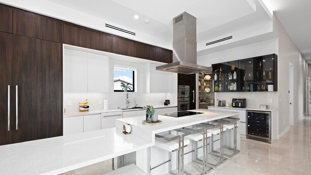 Una cocina moderna con una isla central, taburetes de bar, un enfriador de vino y vistas al exterior.