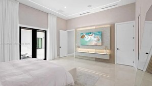 Un dormitorio moderno con una cama grande, un televisor montado en la pared y una puerta corrediza que da a otra habitación.