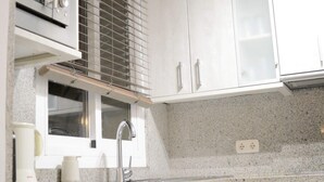 Eine Küche mit weißen Schränken, einer Mikrowelle, einem Spülbecken und einem Fenster mit Jalousien.