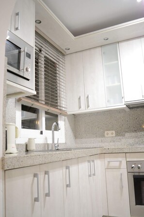 A kitchen with white cabinets, a microwave, a sink, and a window with blinds. - Chalet by the Sea, with private parking, common swimming pools and tennis court (AN)
