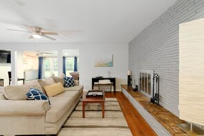 A living room with a sofa, coffee table, fireplace, and a brick wall. - Moody Moon Cottage 3bd with Pool Table 10min dfw (Irving)