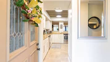 A hallway leading to a kitchen with white cabinets, a tiled floor, and a decorative plant.