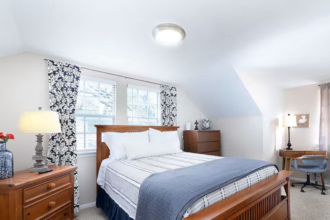 A bedroom with a bed, a desk, a chair, a dresser, and a window with curtains.