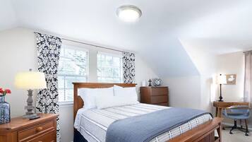 A bedroom with a bed, a desk, a chair, a dresser, and a window with curtains.