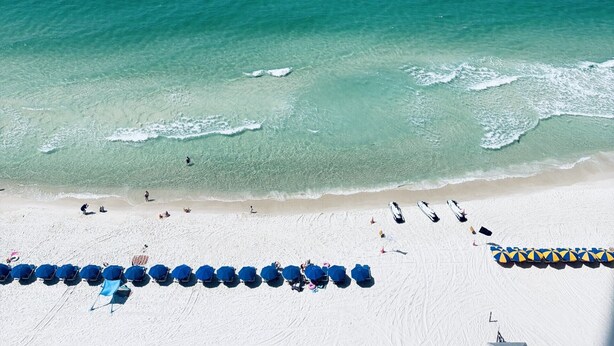 A beach with clear turquoise water, a sandy shore, and rows of blue umbrellas. - New Listing Discount! 1804 W Splash Beach Resort-1BR+Bunks-Gulf Views (Panama City Beach)