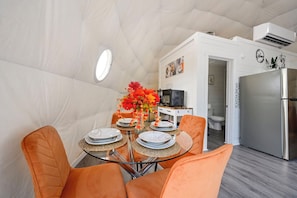 Eine kleine Küche mit Kühlschrank, Mikrowelle und einem Essbereich mit orangefarbenen Stühlen und einem Glastisch.