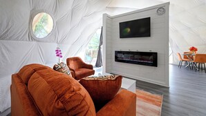 Habitación tipo tienda de campaña con televisor de pantalla plana, chimenea, mobiliario naranja y ventana con vistas.